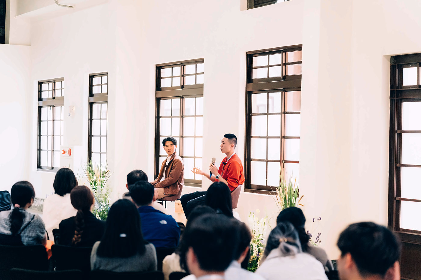 明亮的老建築教室裡，Daniel 和來賓在台前對談，台下坐滿學員
